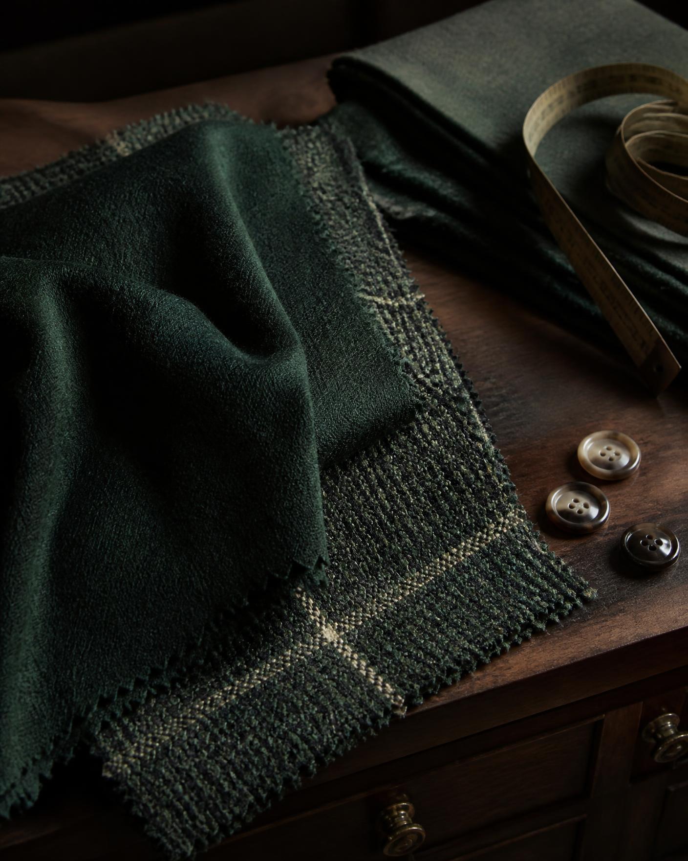 Dark green cashmere and Harris tweed swatches on a walnut tailor's table with horn buttons